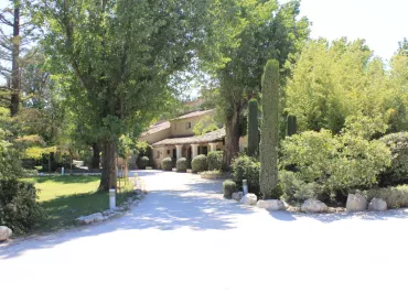Une grande bastide provençale nichée au cœur d’un écrin de verdure, accessible par une allée ombragée.
