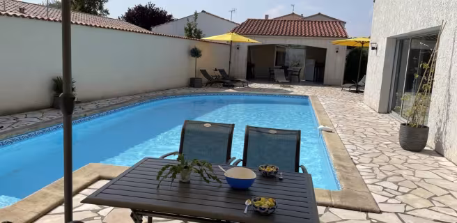 La terrasse avec piscine découverte, un salon de jardin métallique et un parasol sur pied.